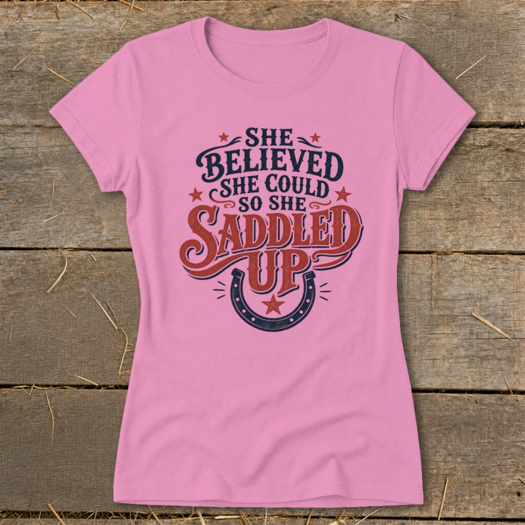 Pink t-shirt with "She believed she could so she saddled up" text and horseshoe graphic.