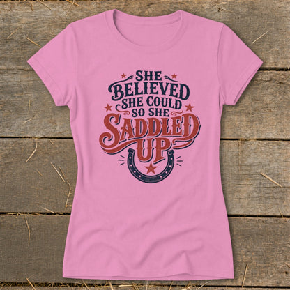 Pink t-shirt with "She believed she could so she saddled up" text and horseshoe graphic.