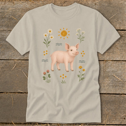 Light tan t-shirt featuring a watercolor illustration of a pink pig surrounded by flowers and sun.