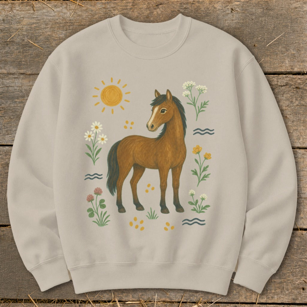 Tan sweatshirt with a brown horse and sun illustration, surrounded by wildflowers and waves.