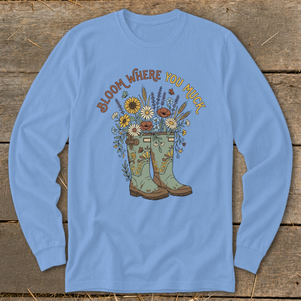 Light blue long sleeve shirt with a floral arrangement in green boots and the text "Bloom Where You Muck".