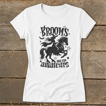 White t-shirt with black graphic of a witch riding a horse, text "Brooms are for amateurs".