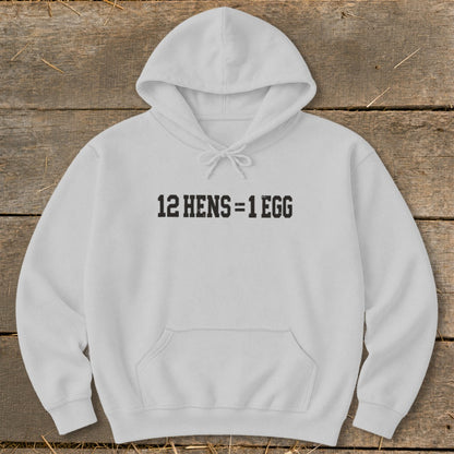 A light gray hooded sweatshirt with the black text 12 HENS = 1 EGG printed on the chest, displayed on a wooden surface.