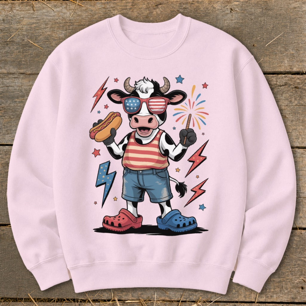 Cartoon cow in patriotic sunglasses holding a hot dog and sparkler.