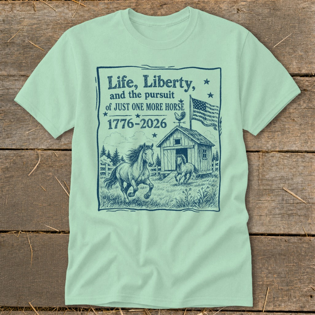 T-shirt graphic with horses, barn, flag, and text "Life, Liberty, and the pursuit of JUST ONE MORE HORSE 1776-2026".