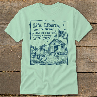 T-shirt graphic with horses, barn, flag, and text "Life, Liberty, and the pursuit of JUST ONE MORE HORSE 1776-2026".