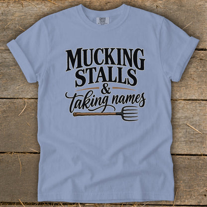 Light blue t-shirt with text "MUCKING STALLS & Taking names" and a pitchfork.
