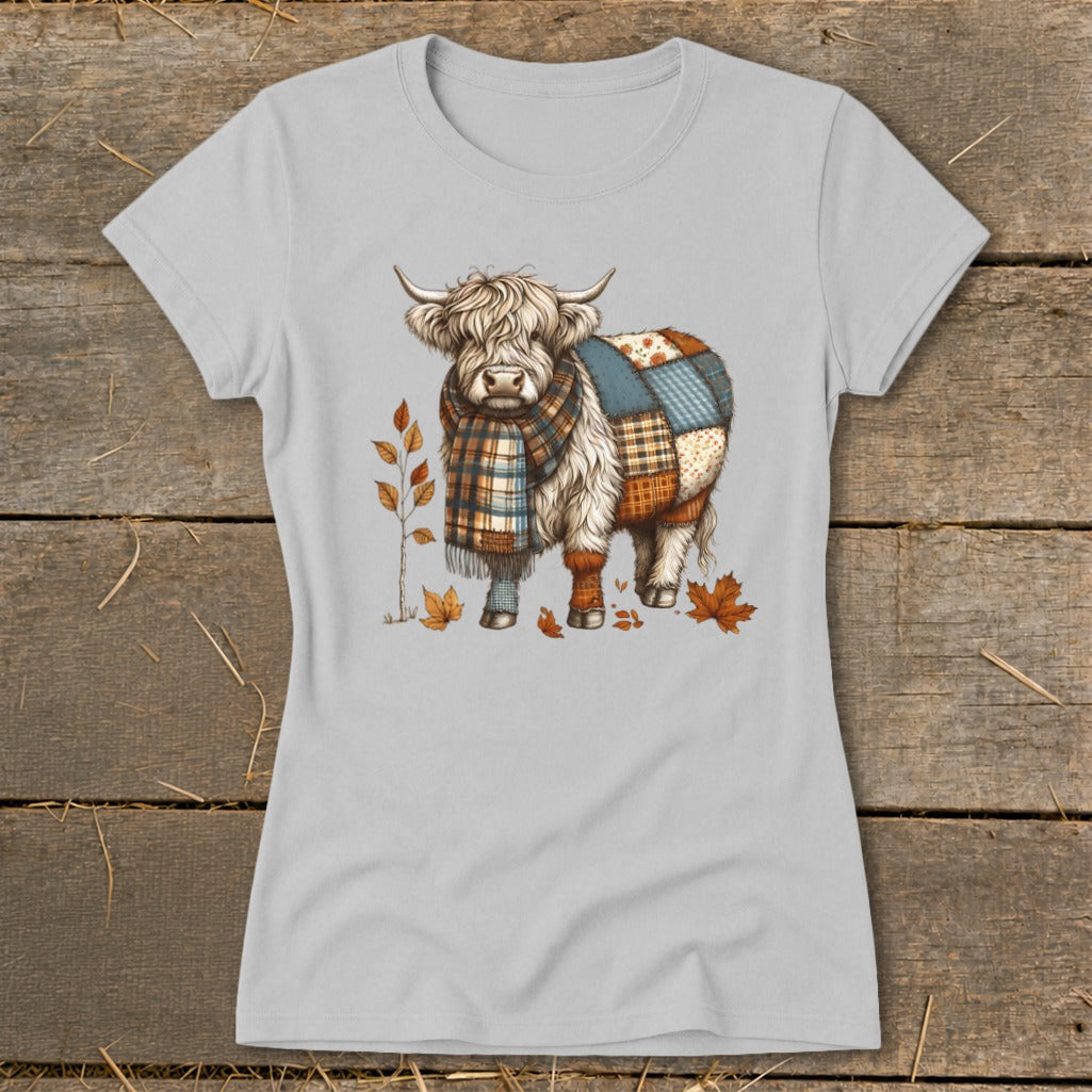 Highland cow wearing a scarf with patchwork pattern, surrounded by autumn leaves.