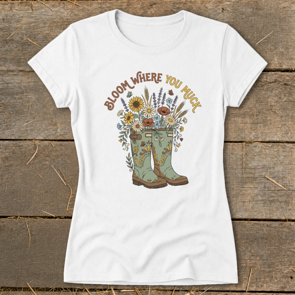 White t-shirt with green boots overflowing with flowers and "Bloom Where You Muck" text.