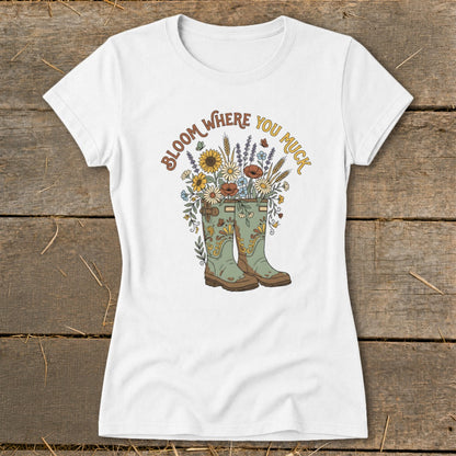 White t-shirt with green boots overflowing with flowers and "Bloom Where You Muck" text.