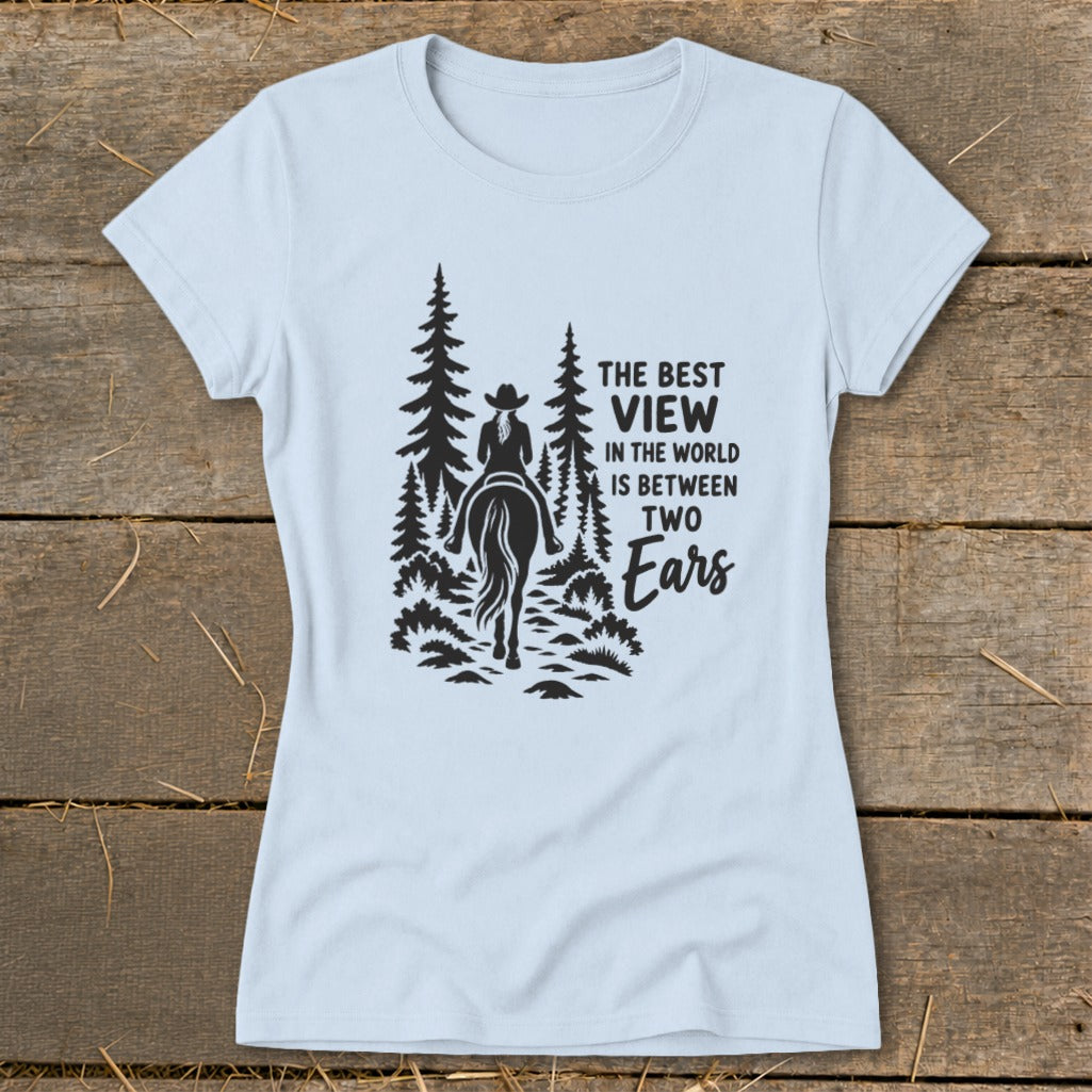 A light blue t-shirt with a black graphic of a horseback rider and trees, featuring the text "The best view in the world is between two ears."