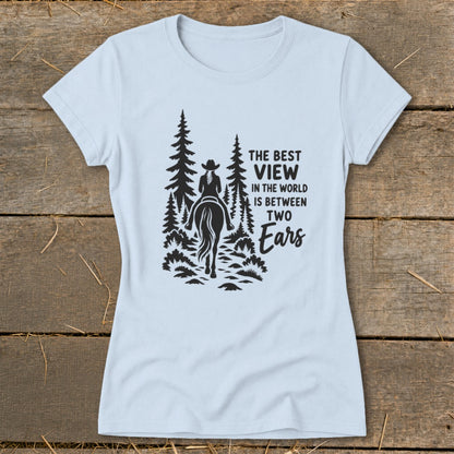 A light blue t-shirt with a black graphic of a horseback rider and trees, featuring the text "The best view in the world is between two ears."