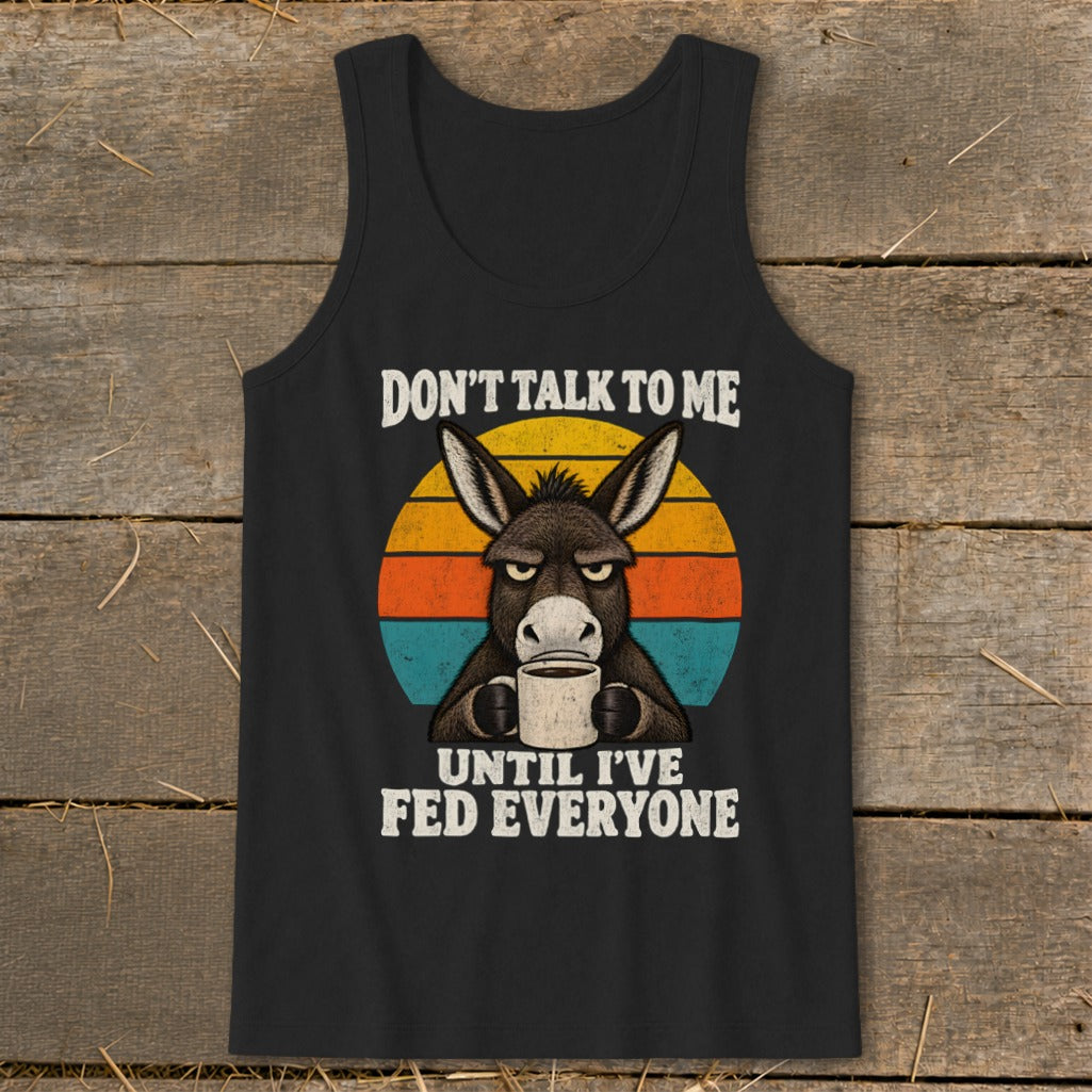A black tank top featuring a graphic of an angry donkey holding a coffee mug against a retro sunset circle, with the text DON'T TALK TO ME UNTIL I'VE FED EVERYONE.