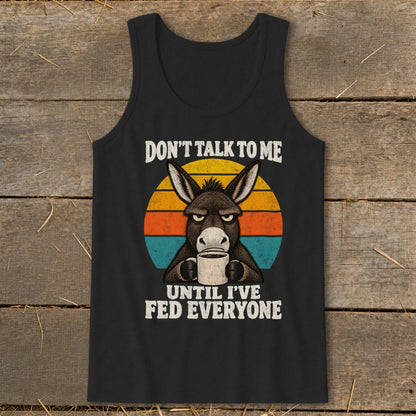 A black tank top featuring a graphic of an angry donkey holding a coffee mug against a retro sunset circle, with the text DON'T TALK TO ME UNTIL I'VE FED EVERYONE.