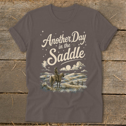 Brown t-shirt with "Another Day in the Saddle" text and cowboy on horseback illustration.