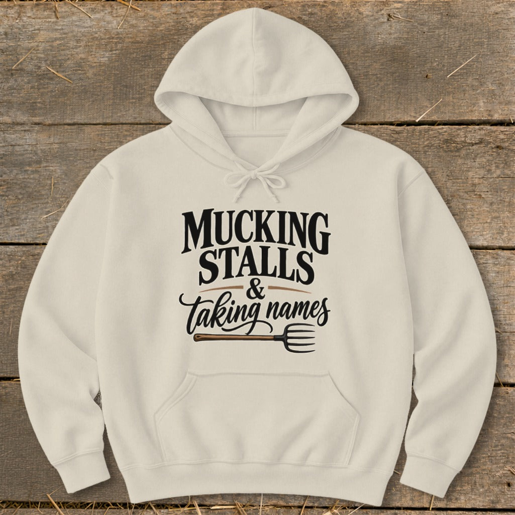 Cream hoodie with "Mucking Stalls & Taking Names" text and a pitchfork graphic.