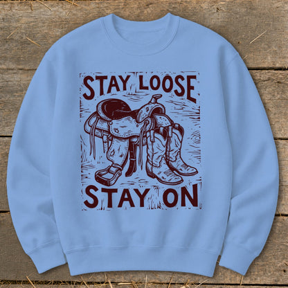 Light blue sweatshirt with maroon graphic of saddle and cowboy boots, reading "STAY LOOSE STAY ON".