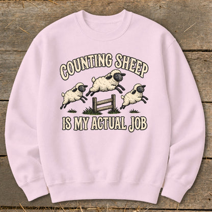 Pink sweatshirt with sheep jumping over a fence and text "COUNTING SHEEP IS MY ACTUAL JOB".