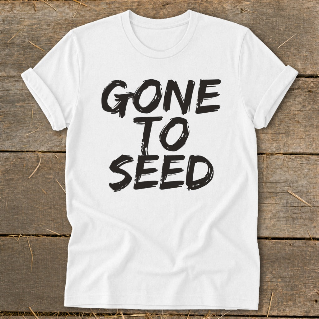 White t-shirt with black text reading "GONE TO SEED" on rustic wooden background.