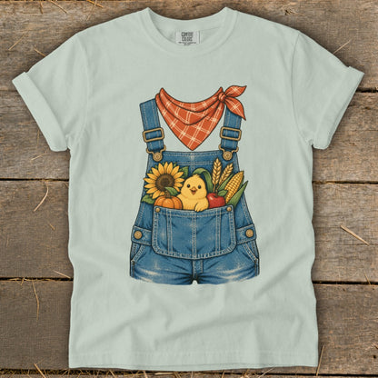 Light blue t-shirt featuring cartoon overalls with a chick and fall harvest elements.