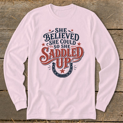 Pink long sleeve shirt with "She believed she could so she saddled up" text and horseshoe graphic.