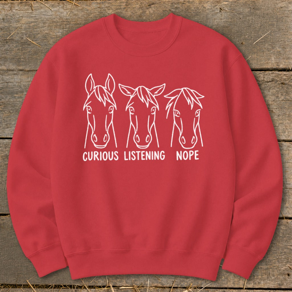 Red crewneck sweatshirt featuring white line art of three horse heads with the text "CURIOUS LISTENING NOPE" underneath.