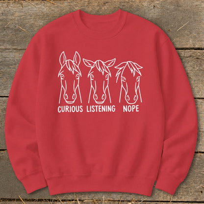 Red crewneck sweatshirt featuring white line art of three horse heads with the text "CURIOUS LISTENING NOPE" underneath.