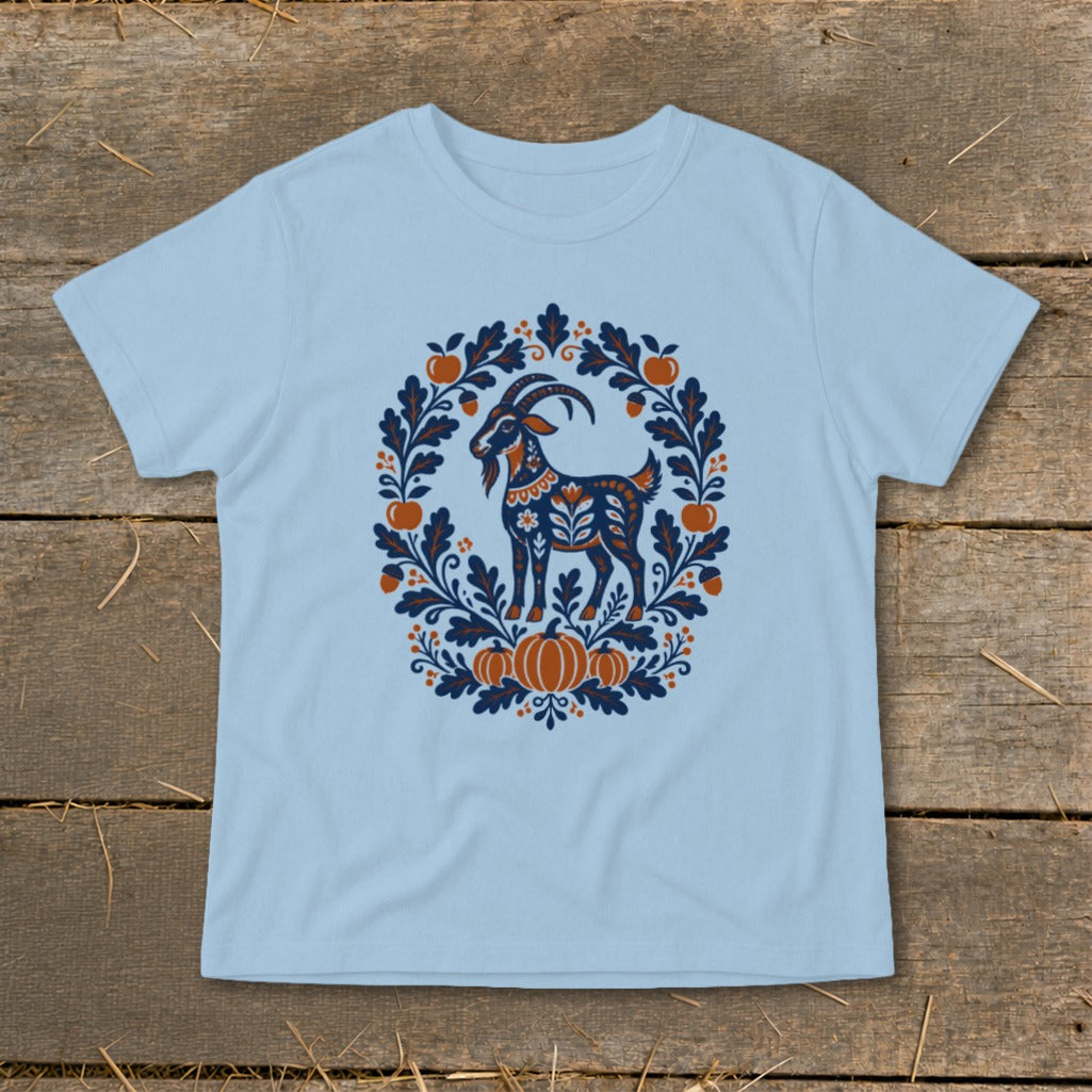 A light blue t-shirt displays a folk art goat graphic surrounded by autumn leaves, acorns, and pumpkins.