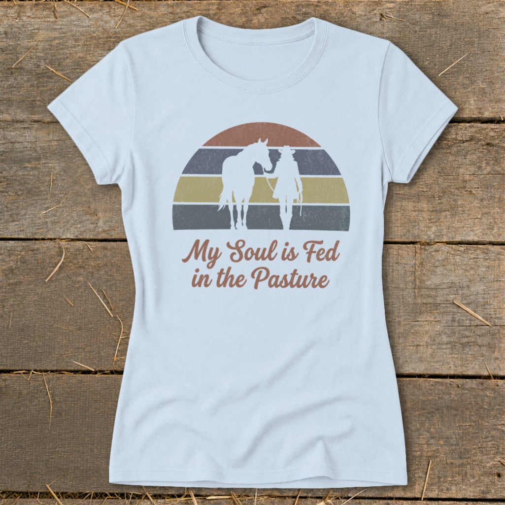 Light blue t-shirt with graphic of a horse and rider silhouette and text "My Soul is Fed in the Pasture".