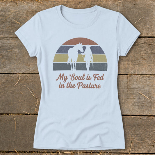 Light blue t-shirt with graphic of a horse and rider silhouette and text "My Soul is Fed in the Pasture".