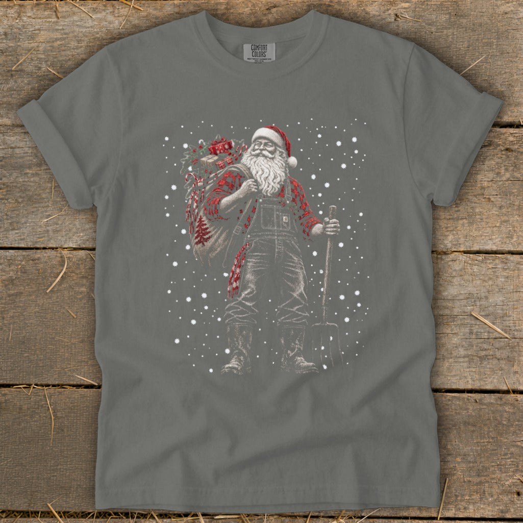 Santa Claus in overalls and plaid shirt carries gifts and shovel in falling snow.