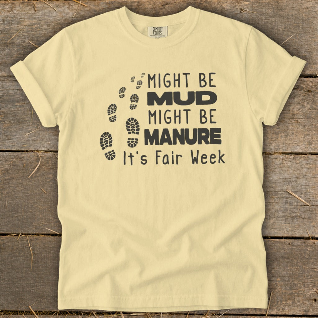 Pale yellow t-shirt with black text and footprints: "Might Be Mud, Might Be Manure, It's Fair Week."