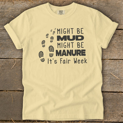 Pale yellow t-shirt with black text and footprints: "Might Be Mud, Might Be Manure, It's Fair Week."