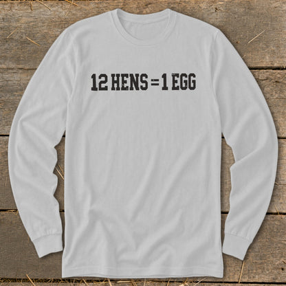 A light gray long-sleeve t-shirt with the black text 12 HENS = 1 EGG printed on the chest, laid flat on a rustic wooden background.