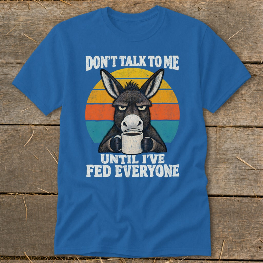 Blue t-shirt featuring a graphic of a grumpy donkey holding a mug against a sunset backdrop.