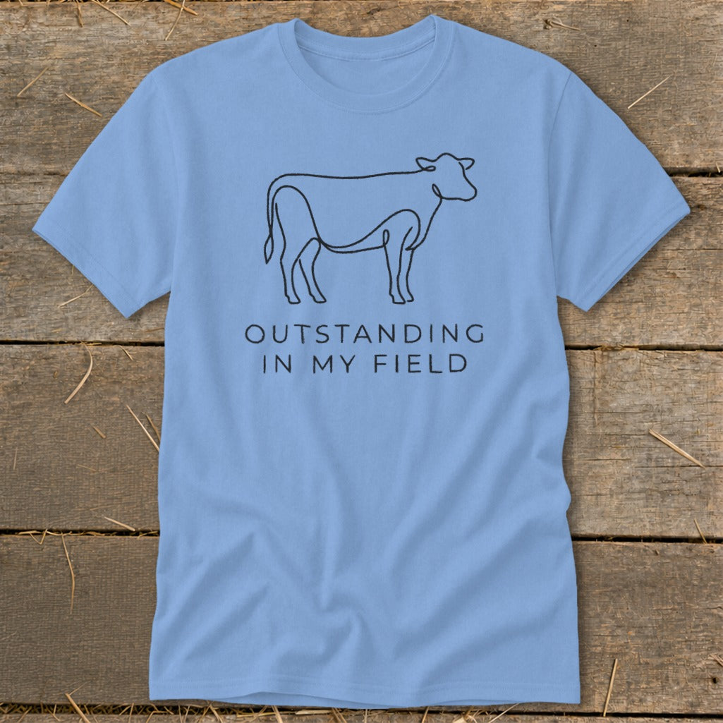 Light blue t-shirt with minimalist cow line art and text "OUTSTANDING IN MY FIELD".