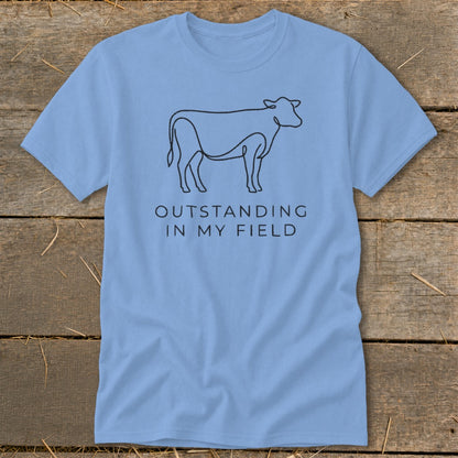 Light blue t-shirt with minimalist cow line art and text "OUTSTANDING IN MY FIELD".