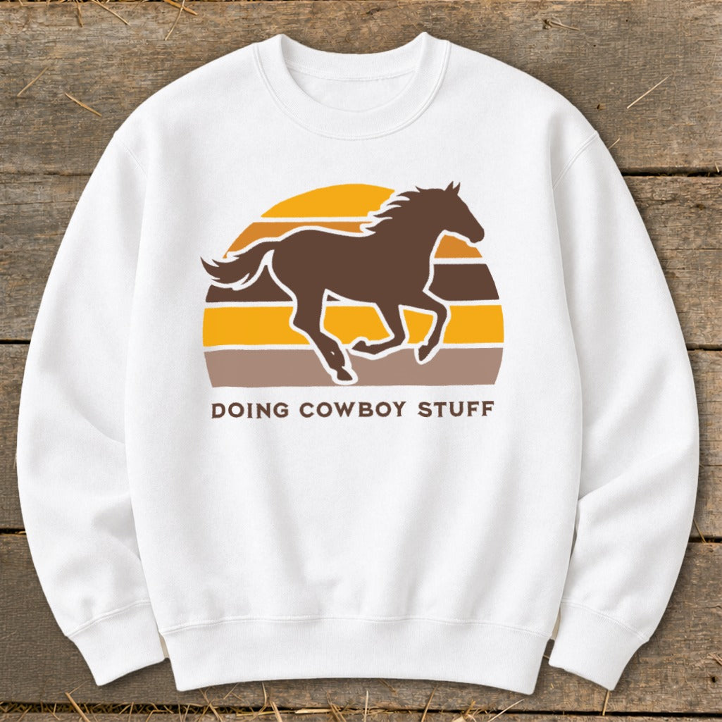 White sweatshirt with brown horse silhouette over striped sunset and "Doing Cowboy Stuff" text.
