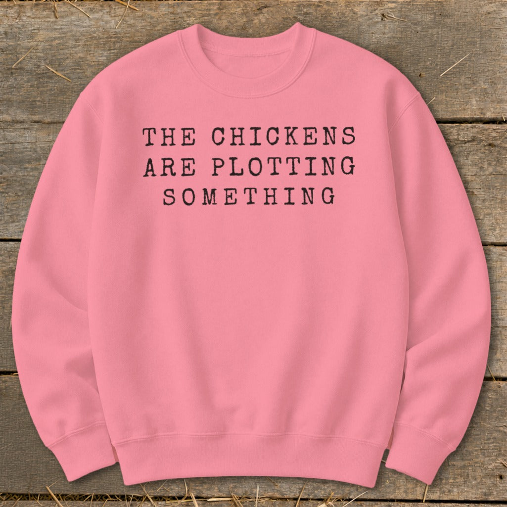 Pink sweatshirt with black text reading "THE CHICKENS ARE PLOTTING SOMETHING."