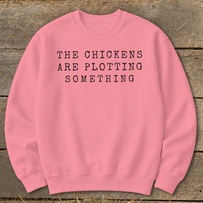 Pink sweatshirt with black text reading "THE CHICKENS ARE PLOTTING SOMETHING."
