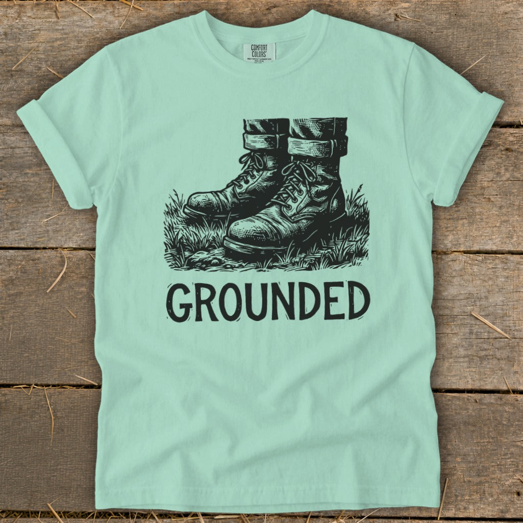 Light blue t-shirt with black graphic of boots in grass and the word "GROUNDED".