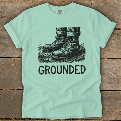 Light blue t-shirt with black graphic of boots in grass and the word "GROUNDED".
