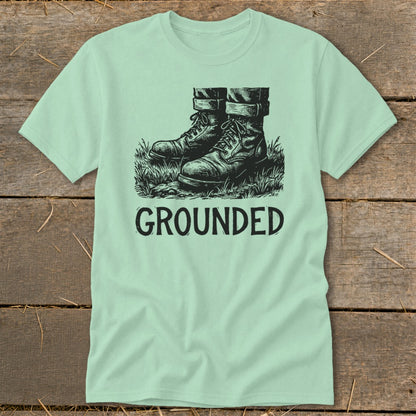 Light green t-shirt with a black graphic of boots in grass and the word GROUNDED.
