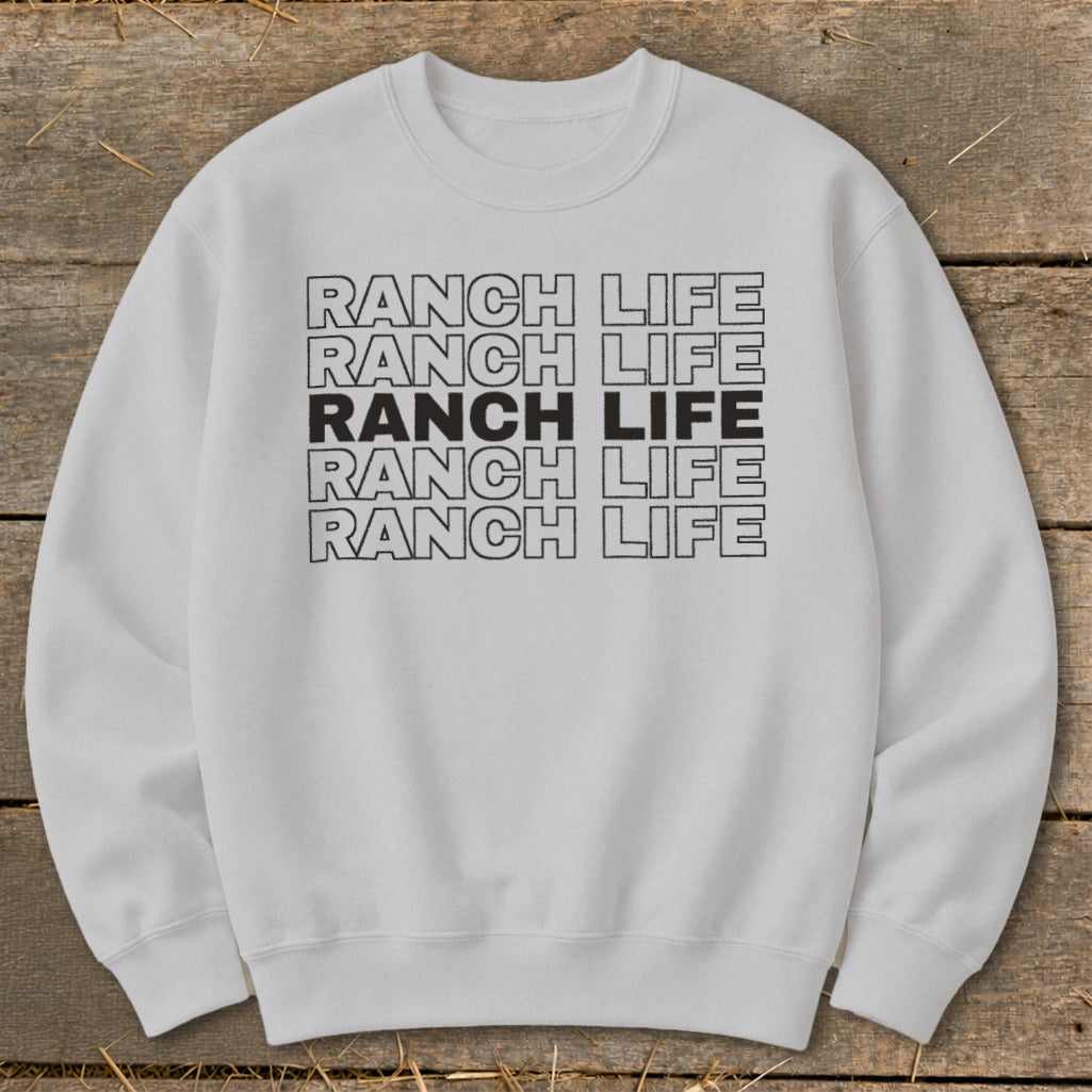 Light gray crewneck sweatshirt featuring five stacked lines of text reading RANCH LIFE on a wooden background.