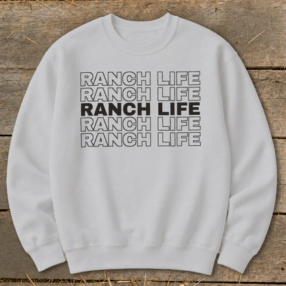Light gray crewneck sweatshirt featuring five stacked lines of text reading RANCH LIFE on a wooden background.