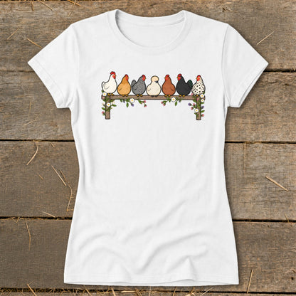 A white short-sleeved t-shirt featuring an illustration of seven colorful chickens perched on a flower-decorated wooden fence.