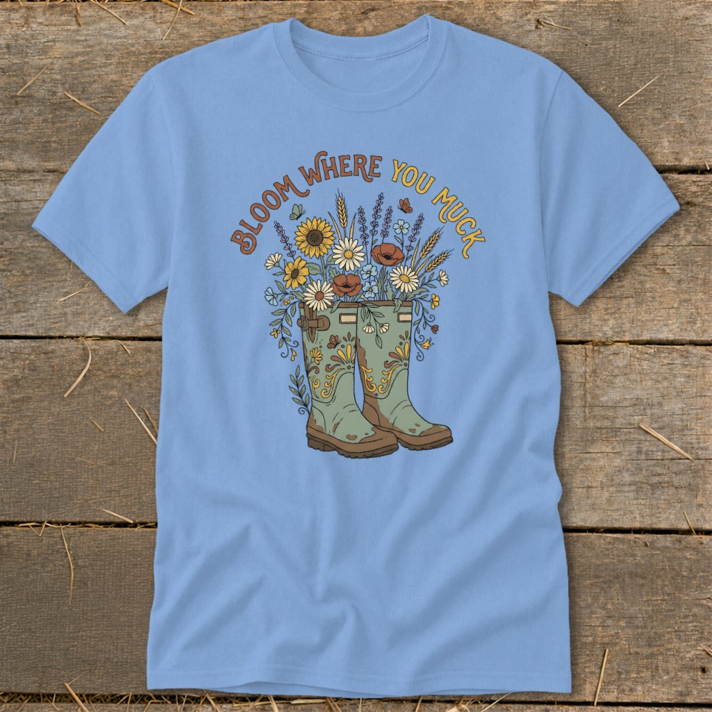Light blue t-shirt with "Bloom Where You Muck" text and garden boots filled with flowers.
