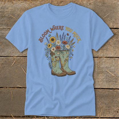 Light blue t-shirt with "Bloom Where You Muck" text and garden boots filled with flowers.