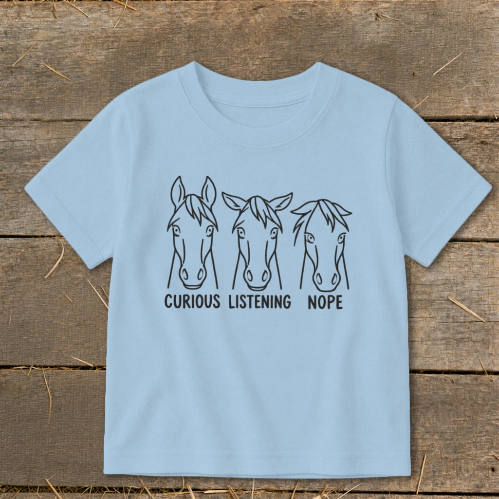 Light blue children's t-shirt featuring three horse head illustrations with the text CURIOUS LISTENING NOPE.