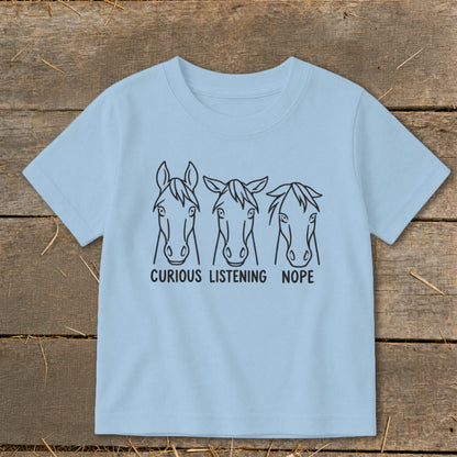 Light blue children's t-shirt featuring three horse head illustrations with the text CURIOUS LISTENING NOPE.
